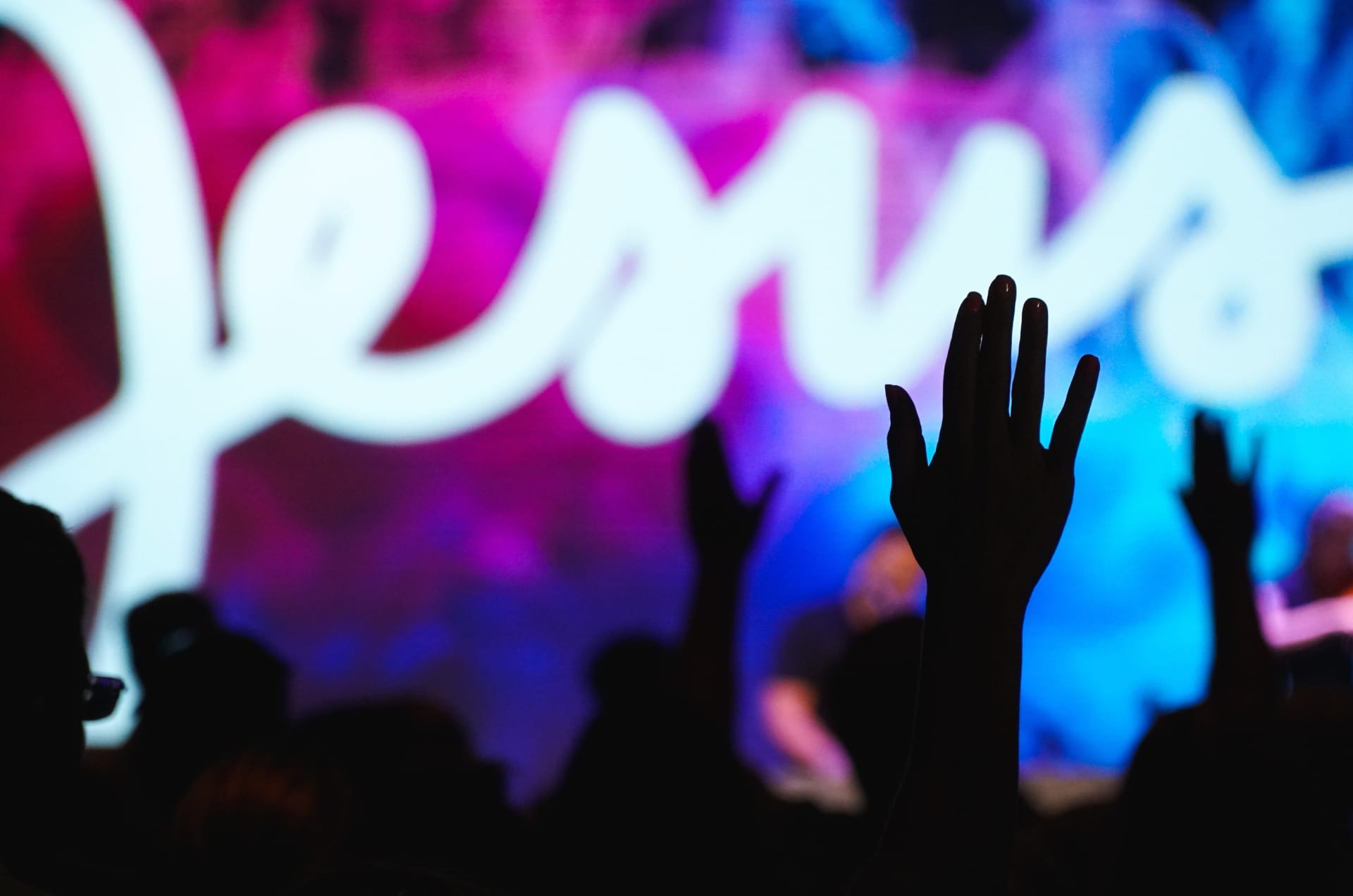 Menschen feiern einen Gottesdienst. Auf der Bühne leuchtet der Name „Jesus“.