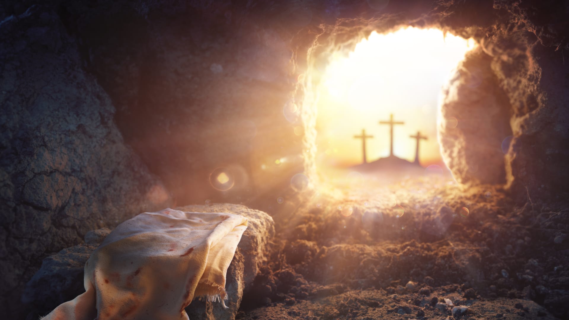 In einer schwach beleuchteten Höhle öffnet sich der Blick auf einen strahlenden Sonnenaufgang, der drei Kreuze auf einem fernen Hügel als Silhouetten erscheinen lässt. Im Vordergrund liegt ein Tuch auf einem Felsen und symbolisiert die Auferstehung von Jesus Christus und die Bedeutung von Ostern.