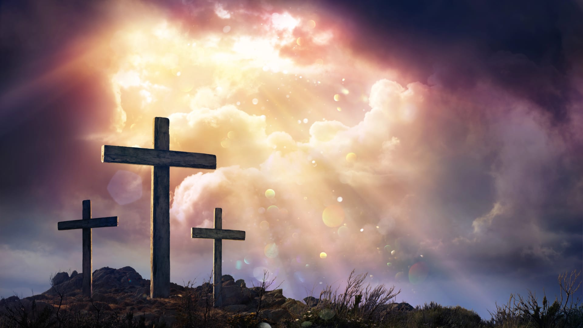 Drei Kreuze stehen auf einem Hügel unter einem dramatischen Himmel, wo Sonnenstrahlen durch dunkle Wolken dringen und ein Gefühl der feierlichen Besinnung auf den Karfreitag hervorrufen.