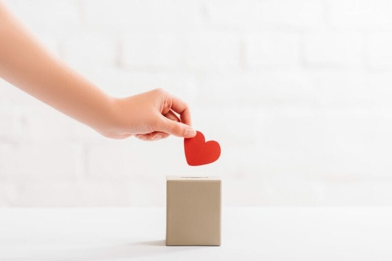 Eine Hand legt ein rotes Herz in eine Spendenbox.